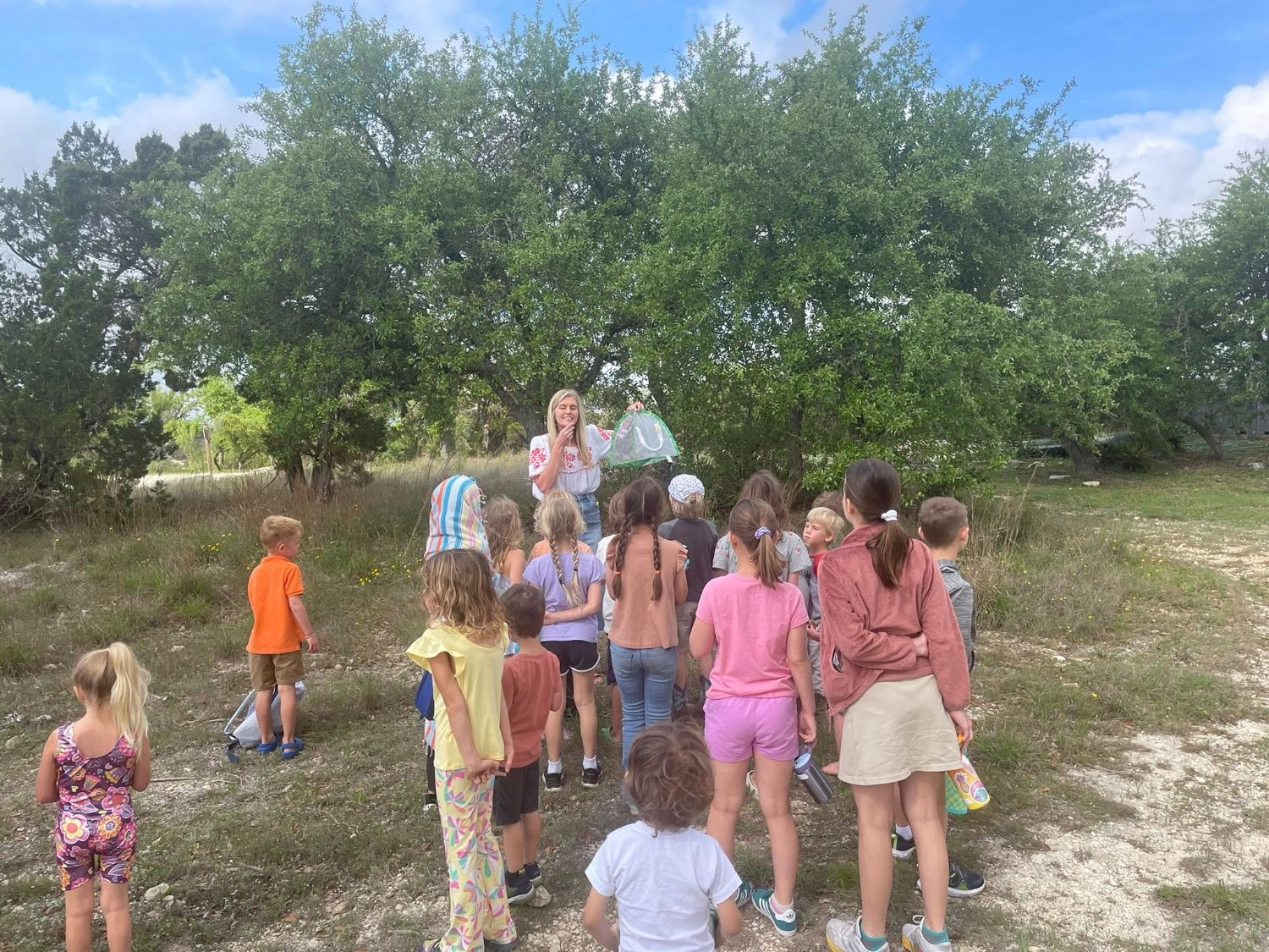 A teacher showing a butterfly habitat to a group of children outdoors