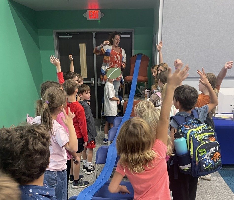 Children raising their hands eagerly around a large blue marble run