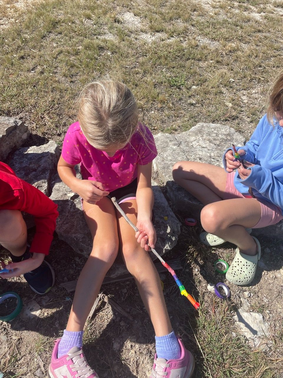 Children decorating nature sticks with colorful tape outdoors