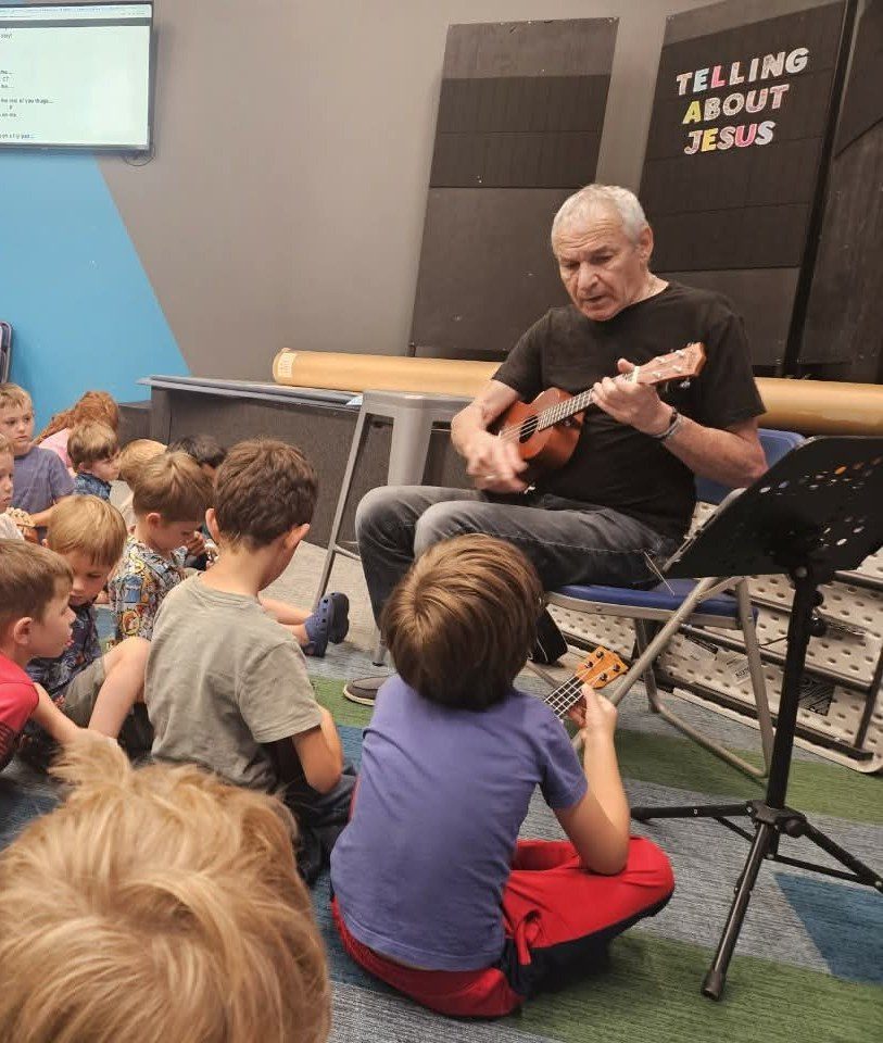 A guest musician playing ukulele for a group of children seated on the floor